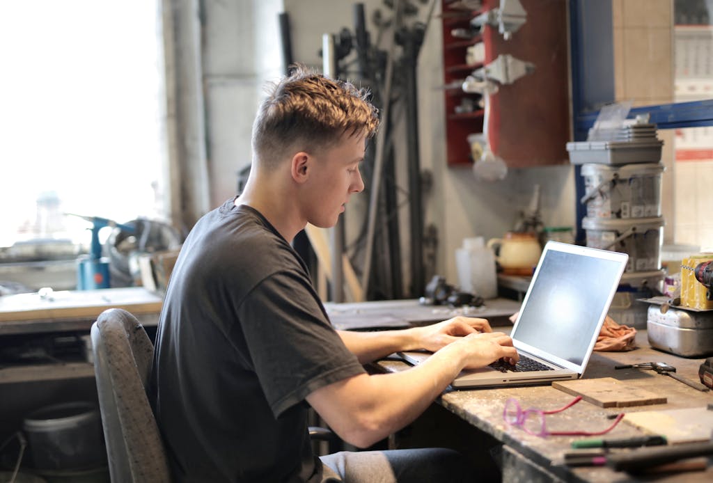 Focused man working remotely from a garage workshop using a laptop.